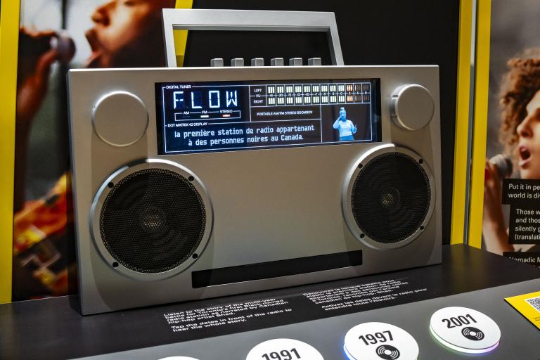 Large boombox-style radio with a screen across the top showing "FLOW", captions and an QSL interpreter. Partially obscured.