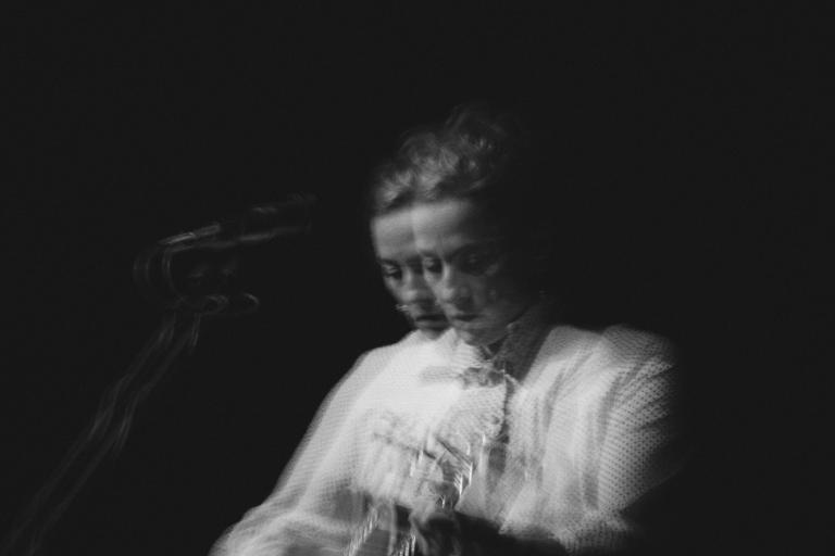 Black-and-white photo of Sarah Harmer playing guitar. It appears like two fuzzy images are juxtaposed one on another. Partially obscured.
