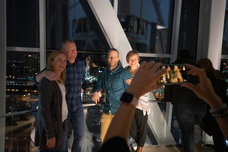 Two smiling couples standing together and posing for a photo in the Museum's tower. Partially obscured.