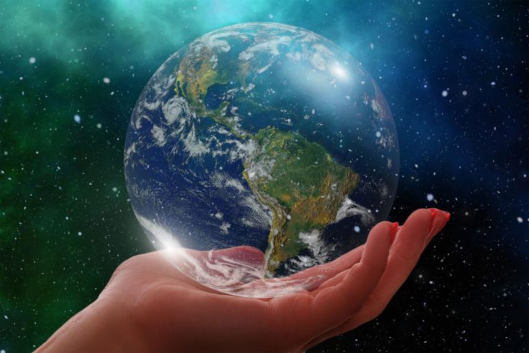 A stylized image shows a human hand gently holding a glass orb of the earth. The background is a night sky with stars and bright green northern lights. Partially obscured.