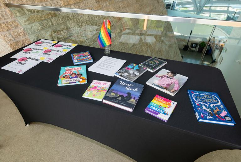 A table with a black tablecloth and colourful books relating to 2SLGBTQI+ Partially obscured.