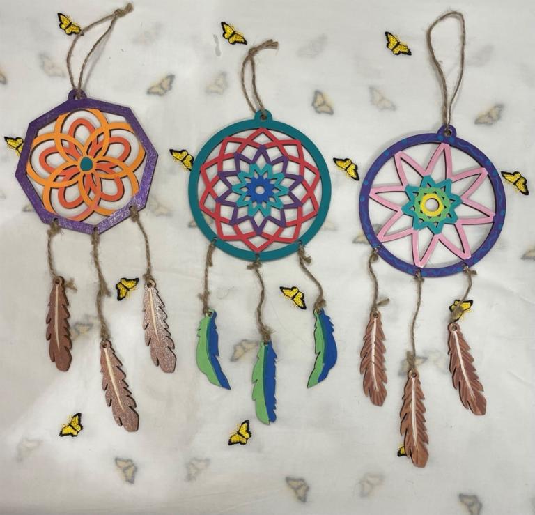 Three colourful dream catchers made from painted wood lie on butterfly-festooned craft paper. Partially obscured.