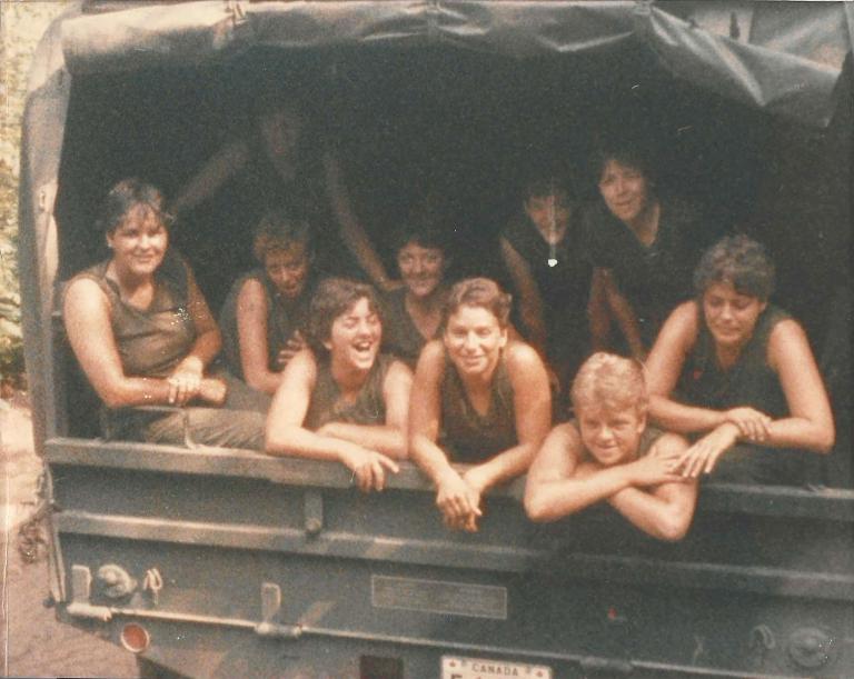 A group of young women in short-sleeved drab green t-shirts smiling.