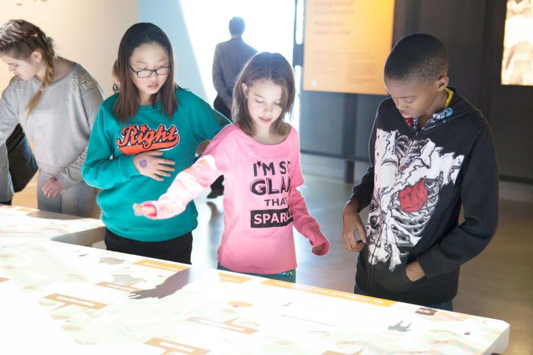 A group of students using an interactive table that is emitting white light. Partially obscured.
