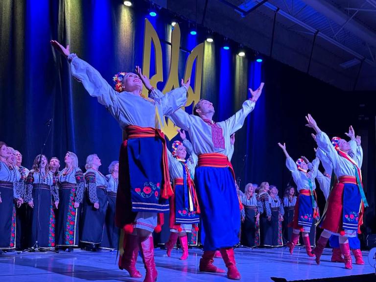 An ensemble of Ukrainian performers dancing on stage; those in the front are looking and reaching up with their arms.