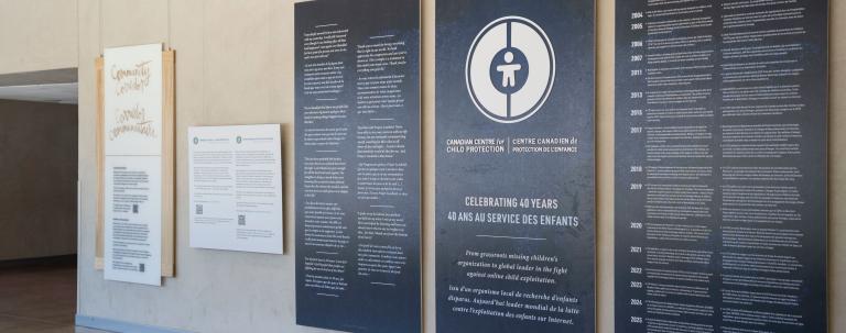 Large dark blue panels with white text and graphics displayed in the Community Corridor at the Canadian Museum for Human Rights. The centre panel features a circular logo and commemorates the 40th anniversary of the Canadian Centre for Child Protection. The two panels on either side present bilingual text in English and French.
