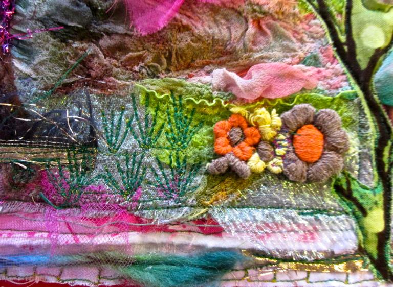 A colourful textile art piece that includes embroidered flowers, branches and greenery mixed with layers of pink, blue and white fabrics. Partially obscured.