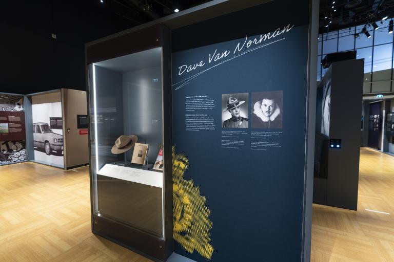 A display case featuring a Stetson hat and magazines is to the left of an exhibition panel with photographs, text, and the words “Dave Van Norman.”