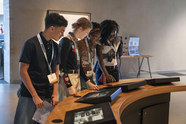 A group of four students interact with screens in a museum gallery. Partially obscured.