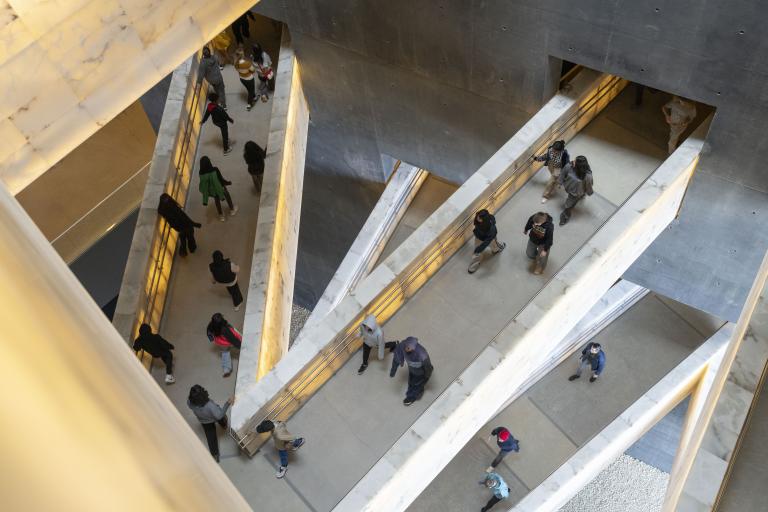 Students walking on ramps that connect various levels of museum galleries. Partially obscured.